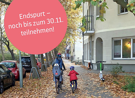 Eine Mutter und ihre Kinder fahren auf einem herbstlich mit Blättern gesäumten Gehweg.