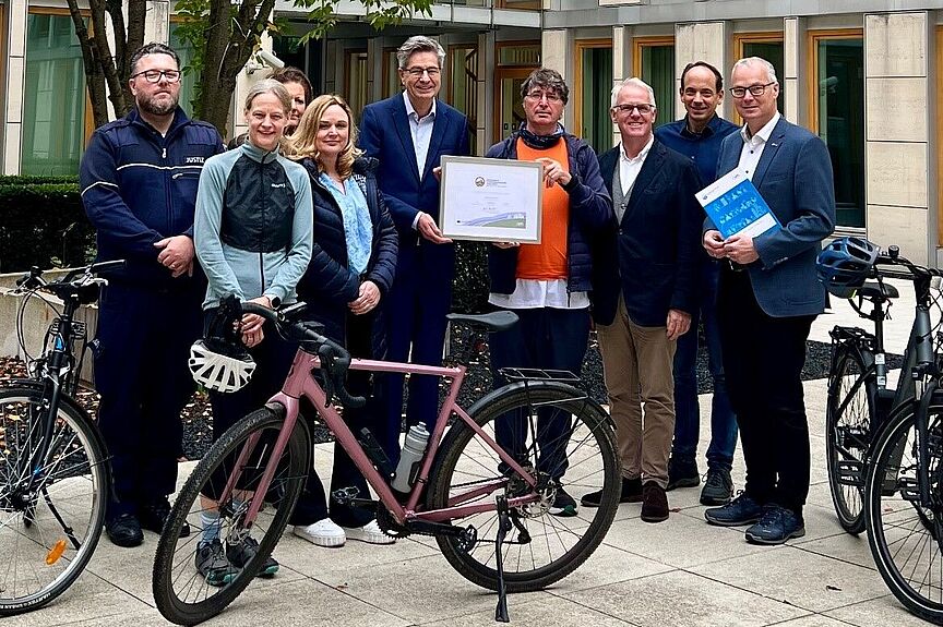 Das Oberlandesgericht Düsseldorf erhält das Gold-Zertifikat als Fahrradfreundlicher Arbeitgeber Gruppe von neun Personen steht vor dem Oberlandesgericht Düsseldorf, in der Mitte wird das gerahmte Gold-Zertifikat „Fahrradfreundlicher Arbeitgeber" präsentiert, im Vordergrund stehen drei Fahrräder.
