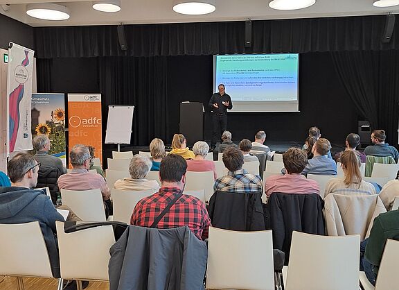 Ein Saal mit Menschen, die dem Vortrag einer Person zu hören.